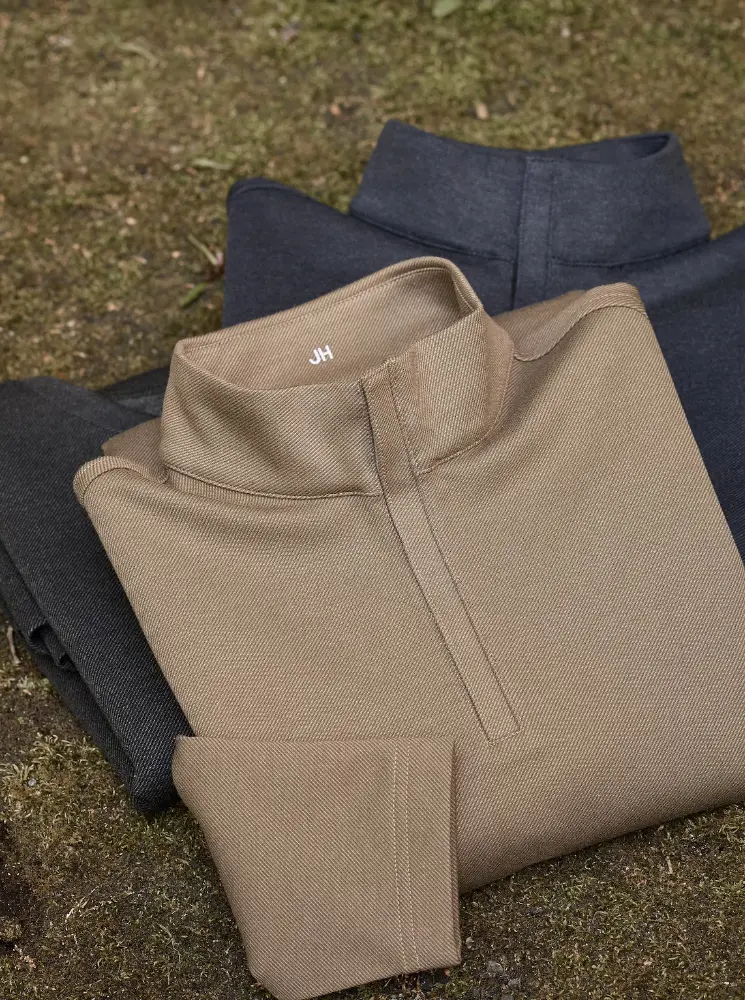 3 neutral shades of mock turtle neck sweaters folded up on grass backdrop