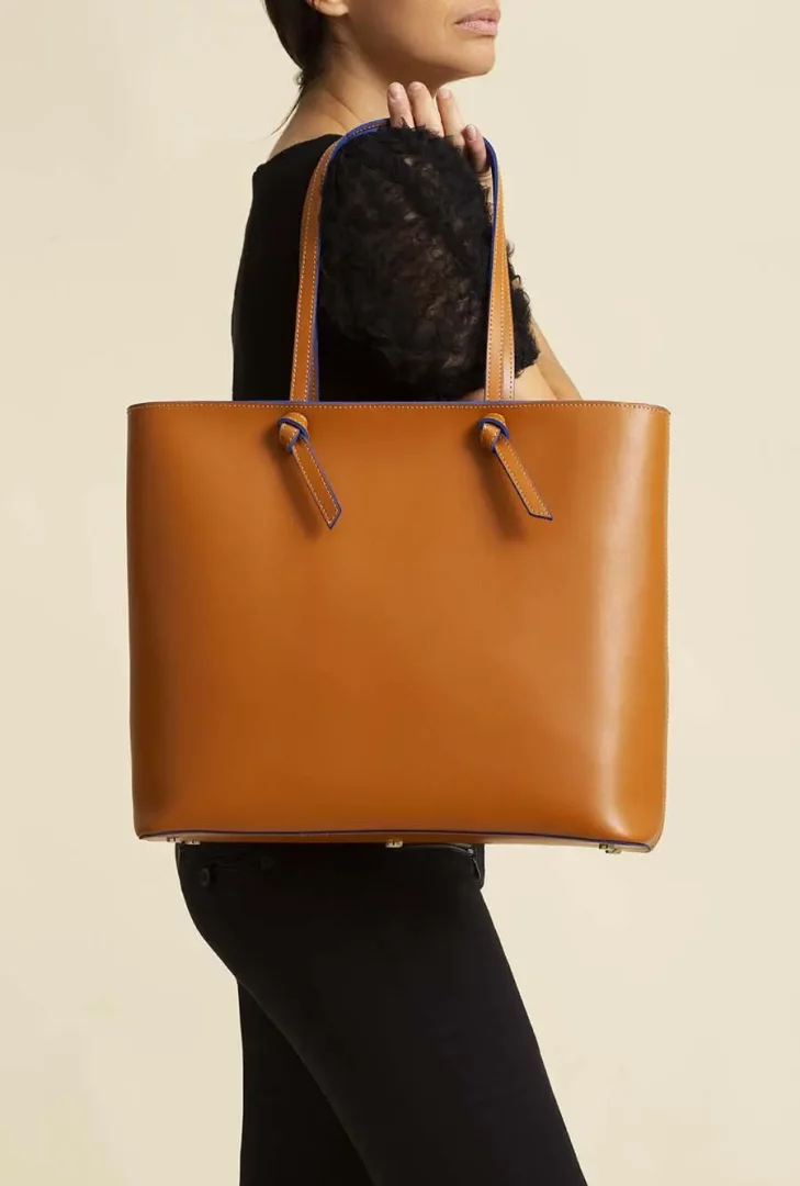 Close up photo of woman in black dress holding a tan leather purse