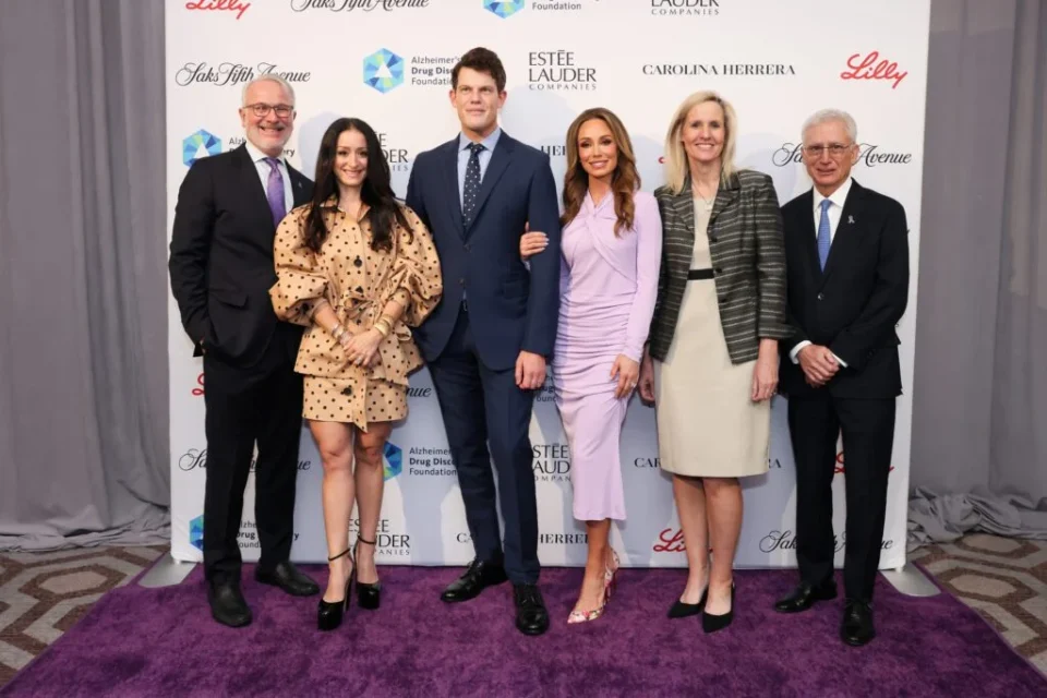 Photo of several people young and old dressed to impress in front of a sponsor wall with logos at a gala event