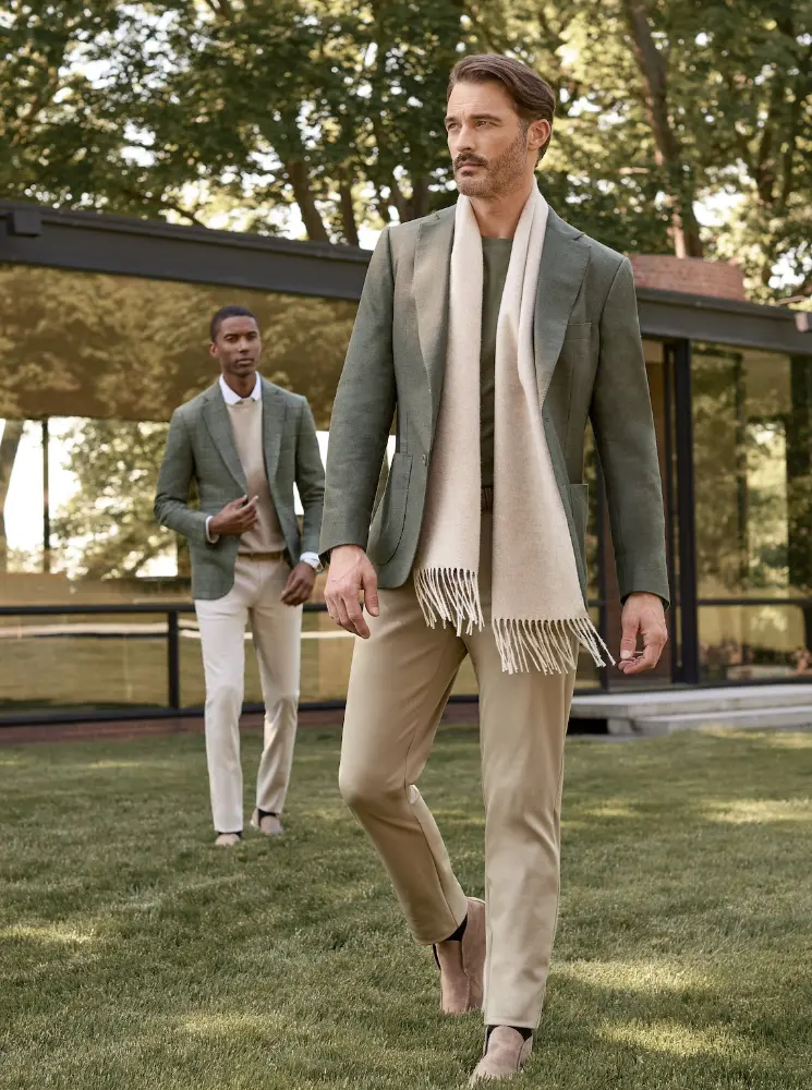 Two young men dressed business casual with soft green blazers walking outside on grass