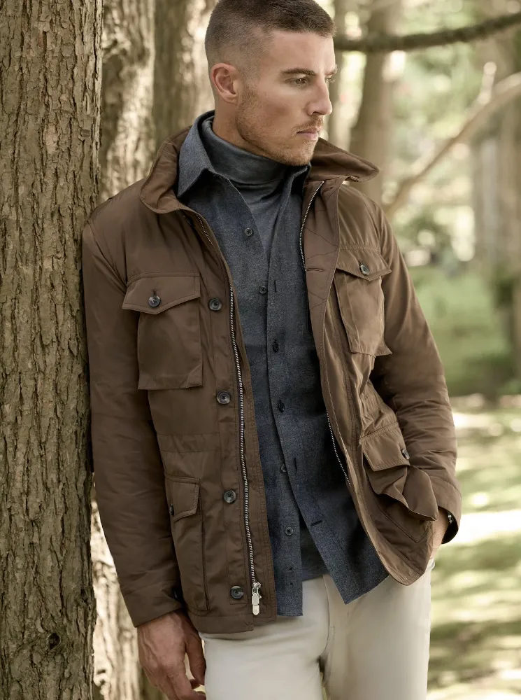 Young man wearing a sport jacket and blue button up shirt leaning against a tree