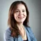 Portrait of Allyson smiling with long brown hair wearing slate blue blazer black blouse and white pearls