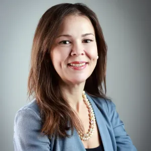 Portrait of Allyson smiling with long brown hair wearing slate blue blazer black blouse and white pearls