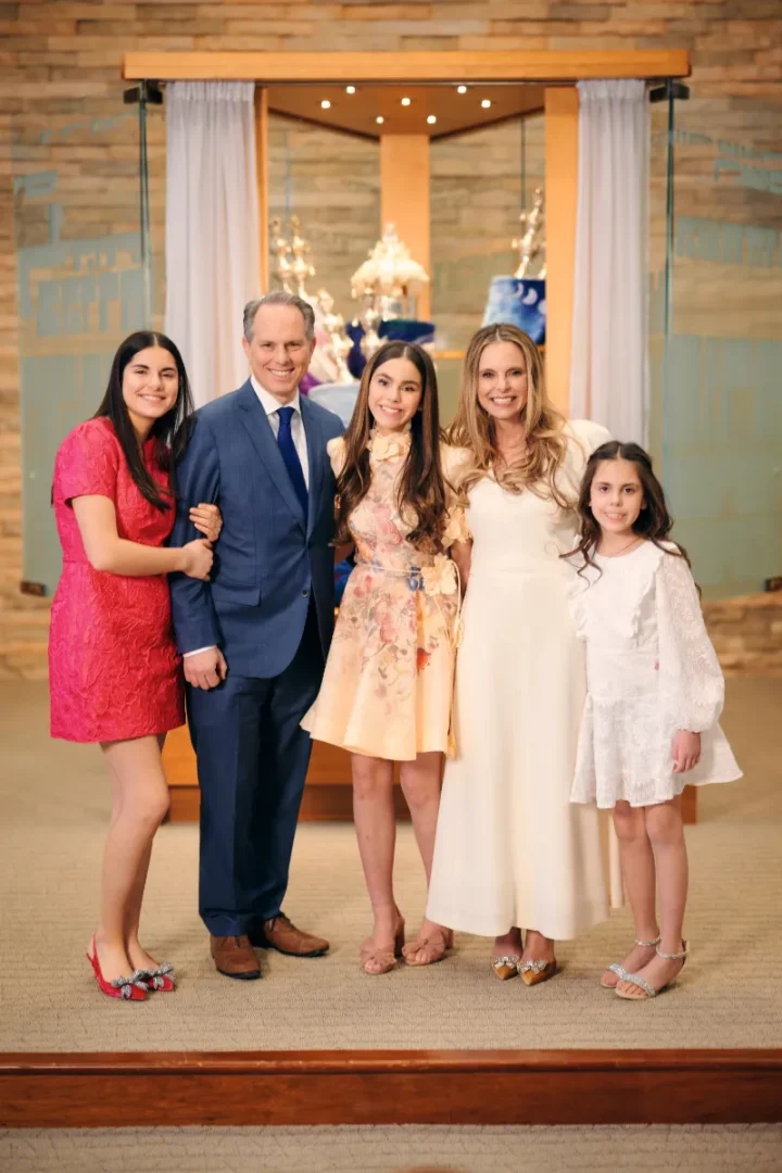 man in blue suit standing with family mom and three daughers in forman dresses.