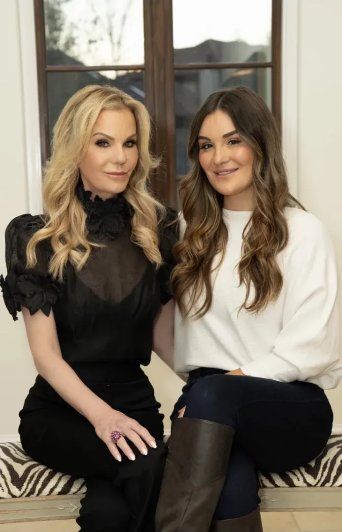 older blonde woman in elegant black dress sitting next to younger woman casually dress with high boots and white sweater