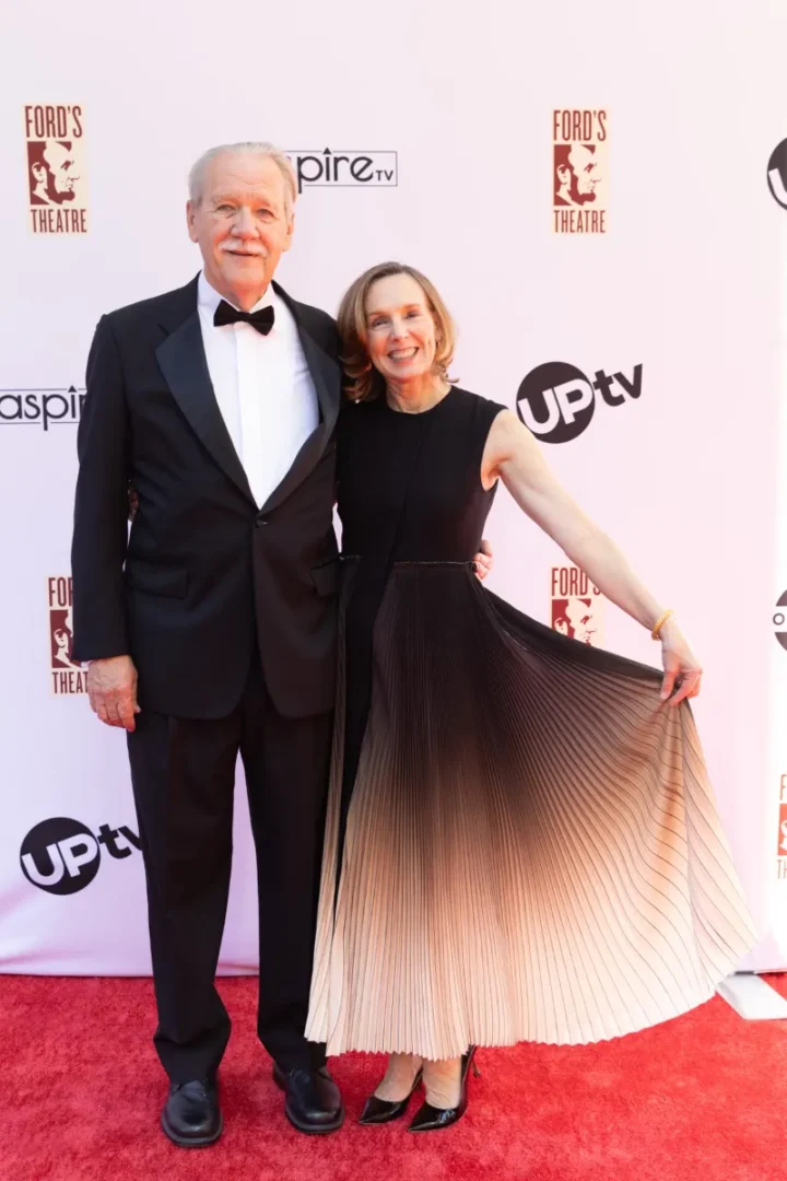 older woman wearing an evening gown next to man wearing a tuxedo at a red carpet event