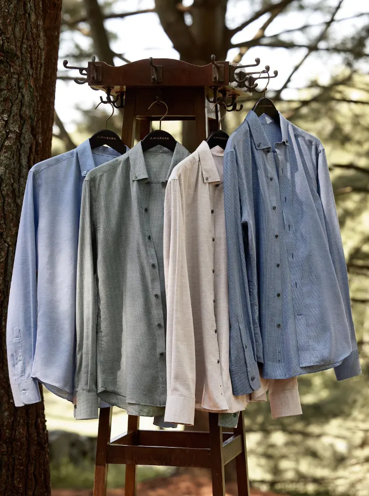 rack of different color button up shirts on hangers outside in the lawn next to a tree